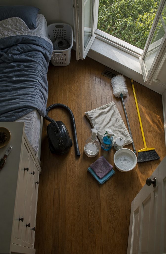 Cleaning supplies beside an open bedroom window with a cloth and spray bottle