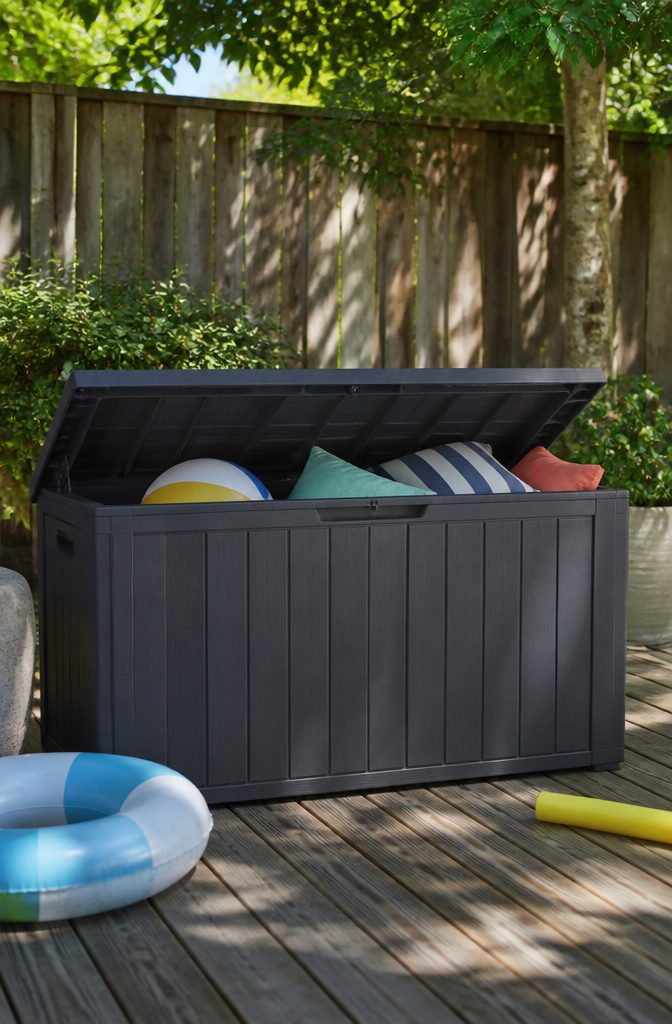 A dark gray resin deck box beside a wall filled with outdoor items.